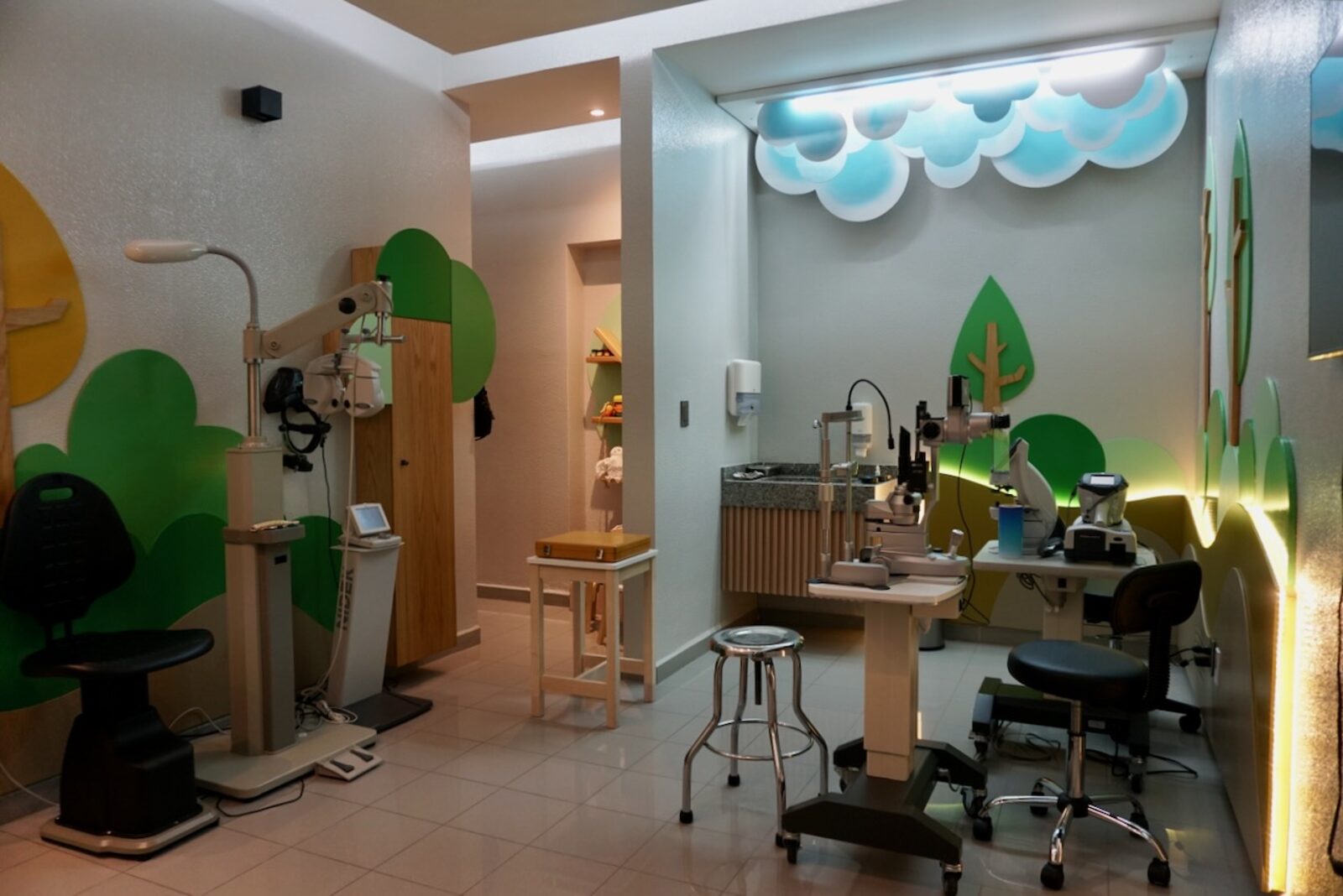 Sala de exploración pediátrica con nubes iluminadas, unidad de refracción y lámpara de hendidura